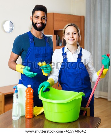 interracial professional couple in uniform cleaning at domestic interior