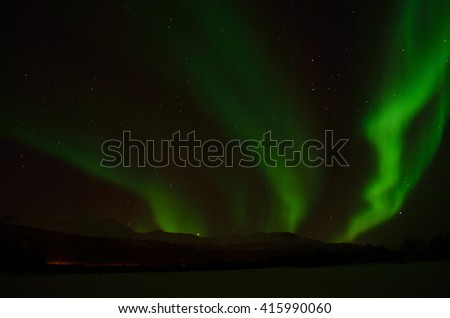 Fantastic vibrant and strong aurora borealis, northern light over snow covered mountain and frozen river bed in the arctic circle at night
