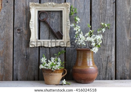 Still life with gorgeous fresh cherry blossom bouquet, bunch branch in clay cup,old Russian ceramic jug, wooden rectangular golden frame, big rusty key, dark background