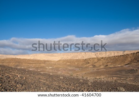 Ramon crater in Israel with scattered prismatic rocks against the cloudy sky
