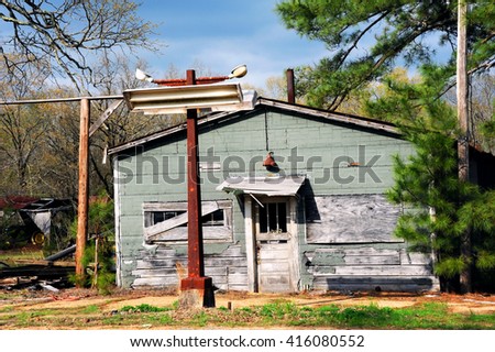 Abandoned country store sits with boarded up windows and rusting sign post.  