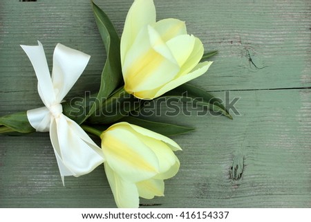 Fresh bouquet of white tulips decorated with white satin ribbon on green vintage wooden background. Floral decor elements