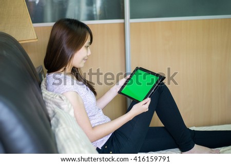 Happy asian girl sitting on bed using a tablet pc with green screen