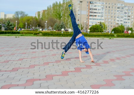 Little boy preparing to do a cartwheel tipping himself to the side on a paved area in an urban park