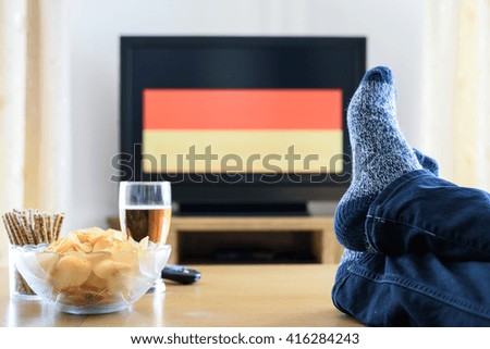 man watching German (Germany) flag on TV screen with legs on table - stock photo