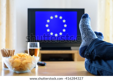 man watching European Union flag on TV screen with legs on table - stock photo