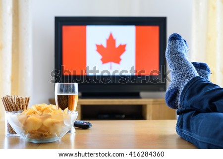 man watching Canadian (Canada) flag on TV screen with legs on table - stock photo