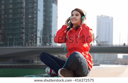 technology, travel, tourism and people concept - smiling young woman or teenage girl in headphones listening to music over dubai city street background