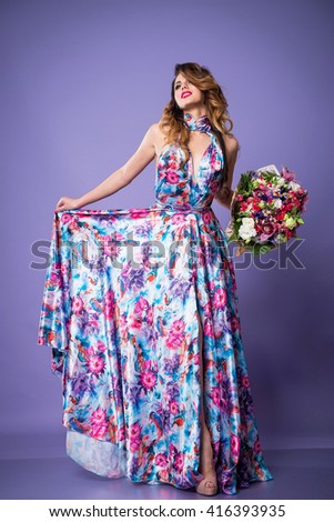 beautiful brunette woman in a bright beautiful dress with flowers on purple background
