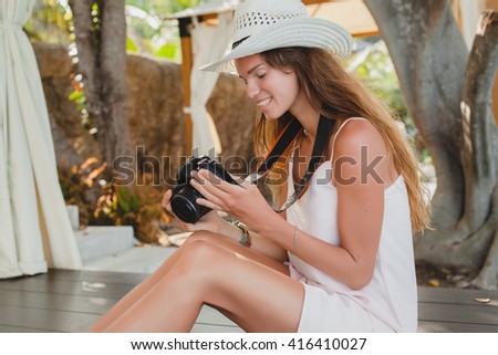 young woman sitting on floor in pale dress, smiling, natural beauty, straw hat, holding digital camera, looking at pictures, tanned skin, slim body, tropical vacation, relaxed, boho style outfit