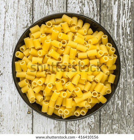 Raw Italian Macaroni Pasta in black bowl with wooden background
