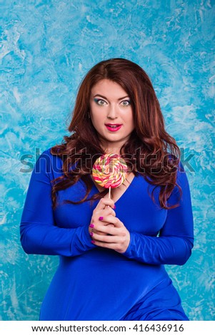 Close-up plump fat plus size redhead woman with long hair, curly with bright makeup and pink lips with sweet candy in hand handmade. Vector blue background. Unusual emotion surprise, shock