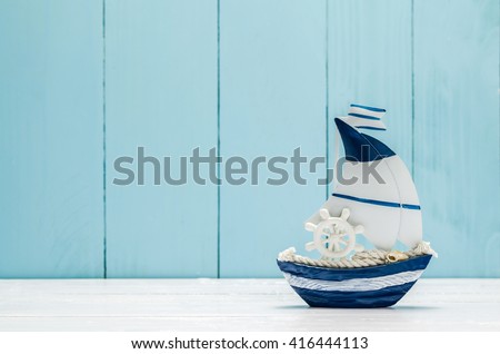 Antique sail boat Toy model with Ship'wheel, rope and seashell on white and blue wooden background - Nautical background Royalty-Free Stock Photo #416444113