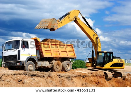 Excavator loading dumper truck tipper in sand pit over blue sky Royalty-Free Stock Photo #41651131