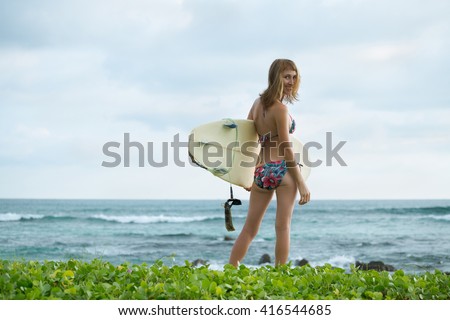 Surfer girl standing with the surf board on the beach and looking at camera