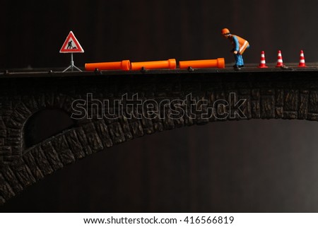 The miniature maintenance  plastic model figure with small orange color pipe put on the model toy bridge represent the maintenance and repair concept related idea.