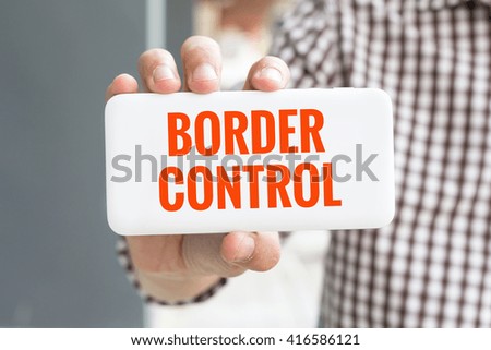 Man hand showing BORDER CONTROL word phone with  blur business man wearing plaid shirt.