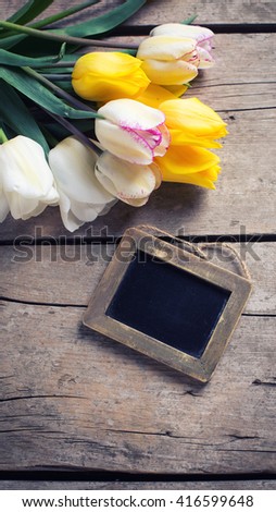 Bright yellow and white spring tulips  and empty blackboard on vintage wooden background. Selective focus. Place for text. Toned image.