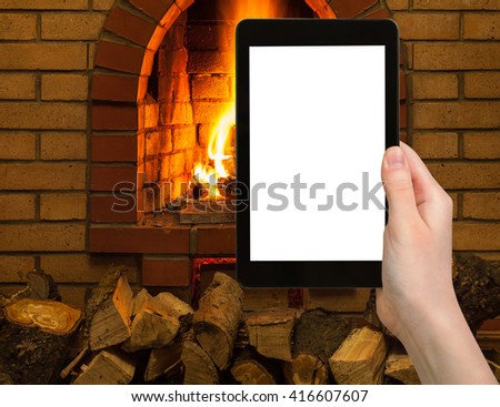 comfortable holiday concept - tourist photographs fireplace on tablet pc with cut out screen with blank place for advertising