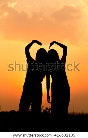 Silhouette heart love sign from girls hand against dusk sunset and sunny golden sky, Friendship together forever concept.