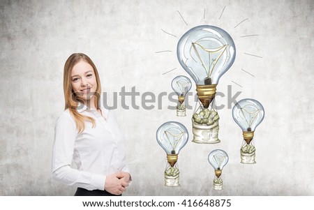 Happy businesswoman standing against concrete wall with lightbulb airballoons and money bags sketch. Success concept