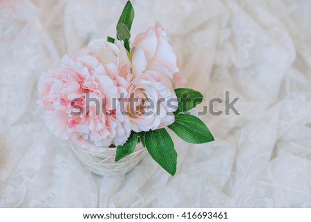 Bouquet of pink peonies in vase. On a table covered with white cloth.