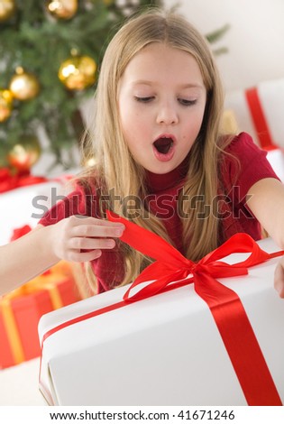 Beautiful teenage girl opening her christmas present. Christmas tree with golden glass balls in background