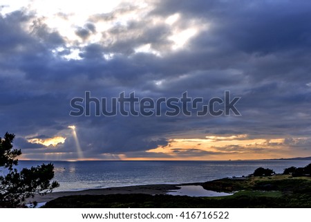 Dramatic cloud opening, the sun appears to burn a hole through the clouds & forms a very bright sunbeam on the ocean. Dark foreboding clouds convey impending danger. Photographed near Cambria CA.
