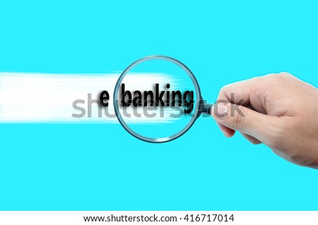 Hand holding magnifying glass focusing on the words e-banking against turquoise background.