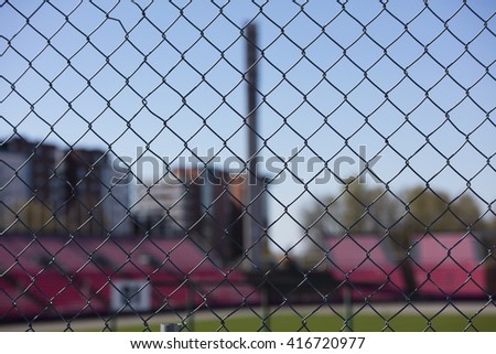 A metal mesh fence in Finland. Sports field and grandstand in the background out of focus. 