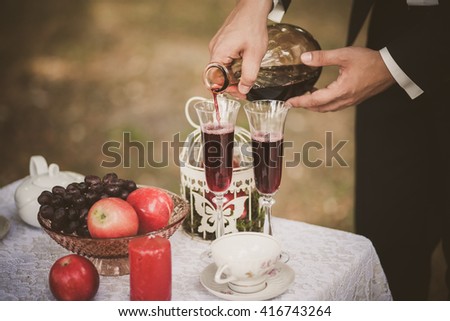 Close up of man hands holding bottle of red wine. Anonymous person pouring drinks in glasses. Man smartly dressed in black suit and white shirt. Preparation for romantic dinner.