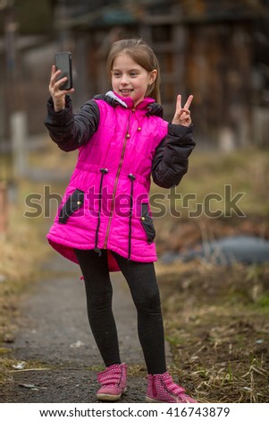 Little girl makes selfie on phone, outdoors.