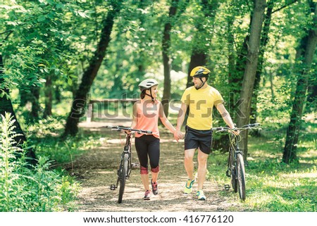 Young couple on weekend holiday, holding hands and walking with bicycles, enjoying nature