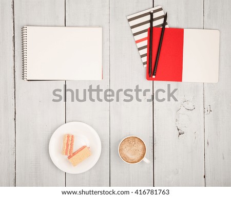 Office table with notepads, cup of coffee and waffles on white wooden background