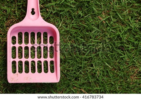 Used and dirty pink color cat litter scooper put on the grass floor represent the pet equipment material concept related idea.
