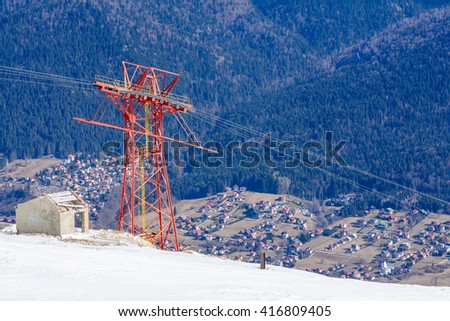 Picture with mountain village from Carpathian Mountains, Romania. Vertical view over mountain village with multiple houses seen from above, snow in front and green firs forest in background.
