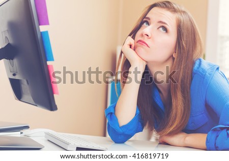 Bored young woman sitting at her desk in front of the computer