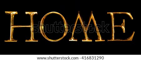 Wooden letters in gold on black background spelling HOME 