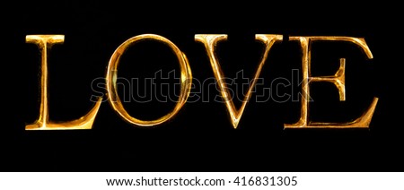 Wooden letters in gold on black background spelling LOVE
