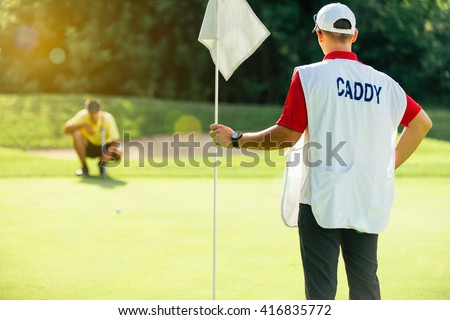 Golf - caddy holding flag, golfer reading green Royalty-Free Stock Photo #416835772