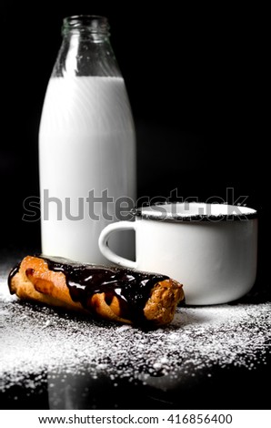 Eclairs with chocolate and milk on a black background with powder