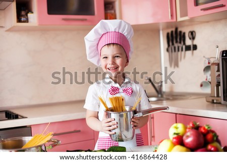 portrait of little boy in the hat of the chef and an apron. Little cooks chef in the kitchen preparing spaghetti. Emotional pictures