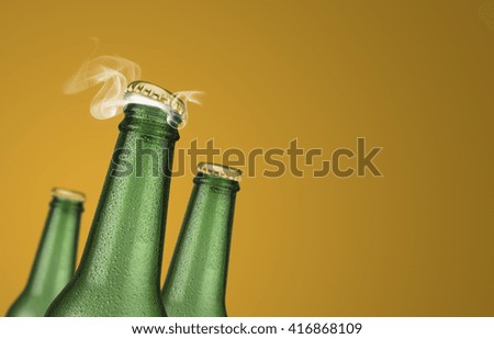 Horizontal photo of three green cold beer bottles with water drops and golden cap open on yellow background