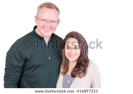 Happy smiling multiracial couple standing arm in arm looking at the camera with warm beaming friendly smiles isolated on white with copy space