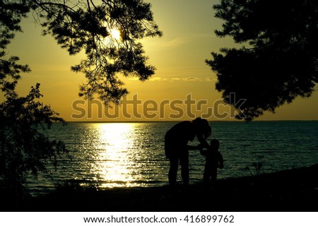 Silhouettes of woman and little boy on the sea beach at sunset 