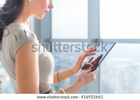 Side view photo of young female teleworker using tablet, searching and browsing information via wi-fi connection application in office or at home. 