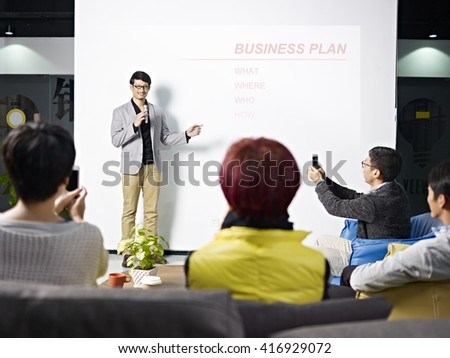 young asian entrepreneur presenting business plan for new project with the audience taking picture with cellphones.