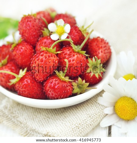 Sweet wild strawberries in plate with daisies on wooden background, selective focus