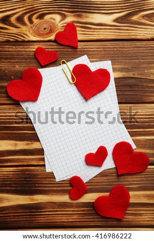 Red hearts and sheet of blank paper on a brown wooden table