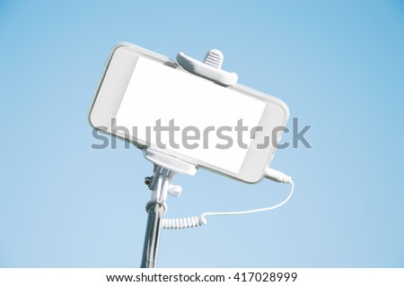 Smart phone with white blank copy space screen for your text or promotional content isolated against blue-sky background. Mobile phone on a selfie stick. Technology and communication concept
